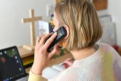 Pfarrerin Nele Schomakers in einem Büro beim Telefonieren - seitlich von hinten aufgenommen mit Blick auf den Bürotisch.  In der linken Hand das Telefon, in der rechten Hand ein Kugelschreiber um Notizen zu machen. Im Vordergrund die Hand und der Telefonhörer am Ohr.